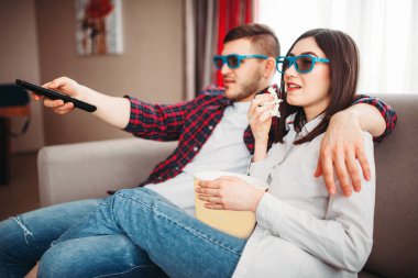 Genç çift kanepede oturan ve evde, patlamış mısır adamla uzaktan kumanda ile tv izlerken 3d gözlük 