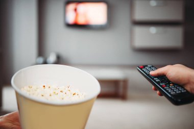 Televizyon uzaktan kumanda ve Tv karşı patlamış mısır duvardaki erkek elleriyle. Ev eğlence kavramı