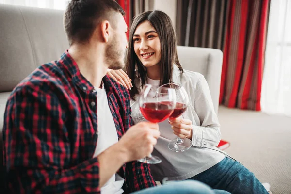 love couple sitting on the floor against couch, drinking red wine, romantic evening