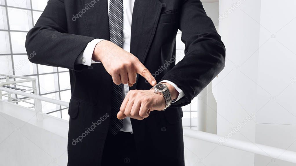 young businessman in black suit pointing a finger at watch