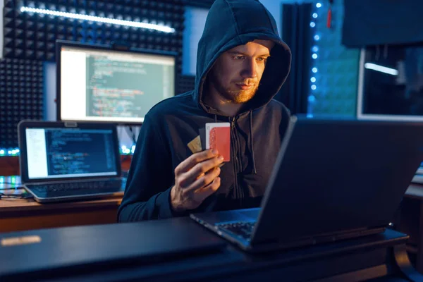 フードのハッカーはノートパソコンやデスクトップPc パスワードや金融ハッキング ダークネットユーザーと彼の職場で銀行のクレジットカードを示しています インターネットスパイ犯罪生活リスク仕事ネットワーク犯罪者 — ストック写真