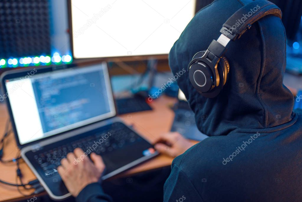 Hacker in the hood sitting at laptop, back view, information hacking. Internet spy, male programmer trying to hack an encrypted network