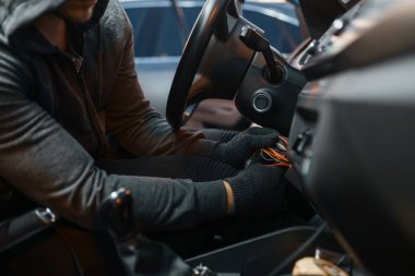 Profesyonel araba hırsızı kontak kilidi, suç dolu bir yaşam tarzı. Kapüşonlu erkek soyguncu park yerindeki araç güvenlik sistemini aştı. Otomobil soygunu, otomobil suçu