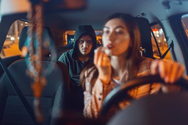 Kadın sürücü ve kapüşonlu araba hırsızı arka koltukta, suç yaşam tarzı, hırsızlık. Erkek haydut ve otoparktaki araçta kurban. Araba soygunu, otomobil suçları, uçak kaçırma.