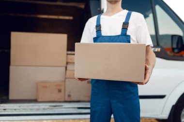 Karton kutulu teslimatçı, teslimat servisi. Üniformalı bir adam karton bir paket taşıyor, erkek teslimatı, kurye işi.