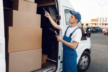 Üniformalı teslimatçı. Posta kutuları, teslimat servisi. Karton paketlerin başında duran bir adam araç, erkek teslimatı, kurye ya da nakliye işi