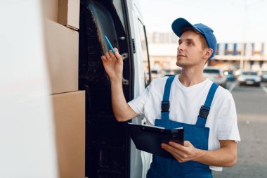 Üniformalı teslimatçı. Posta kutuları, teslimat servisi. Aracın içinde karton paketlerin başında duran adam, erkek teslimat...