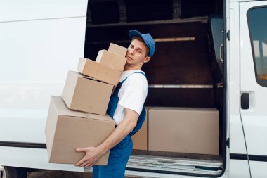 Üniformalı postacı paketleri, teslimat hizmetlerini arabaya boşaltır. Karton paketlerin başında duran bir adam araç, erkek teslimatı, kurye ya da nakliye işi
