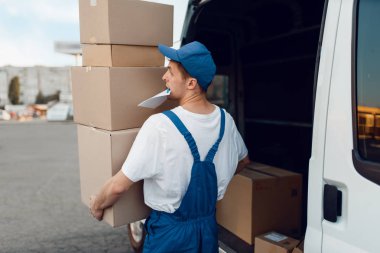 Üniformalı postacı paketleri, teslimat hizmetlerini arabaya boşaltır. Karton paketlerin başında duran bir adam araç, erkek teslimatı, kurye ya da nakliye işi