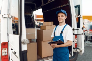 Üniformalı teslimatçı arabada paket kutuları ve teslimat servisiyle poz veriyor. Karton paketlerin başında duran bir adam araç, erkek teslimatı, kurye ya da nakliye işi