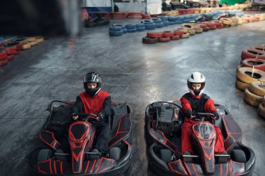 Başlangıç çizgisinde iki kart yarışçısı, ön görüş, kapalı alanda karting otomobil sporu. Lastik bariyeriyle yakın go-cart pistinde hız yarışı. Hızlı araç yarışması, yüksek adrenalin eğlencesi.