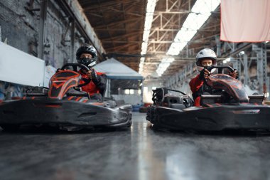 İki kart yarışçısı galibiyet için kucak, yan görüş, kapalı alanda karting otomobil sporu. Lastik bariyeriyle yakın go-cart pistinde hız yarışı. Hızlı araç yarışması