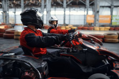 İki kart yarışçısı galibiyet için kucak, yan görüş, kapalı alanda karting otomobil sporu. Lastik bariyeriyle yakın go-cart pistinde hız yarışı. Hızlı araç yarışması, yüksek adrenalin eğlencesi.