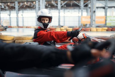 İki kart yarışçısı galibiyet için kucak, yan görüş, kapalı alanda karting otomobil sporu. Lastik bariyeriyle yakın go-cart pistinde hız yarışı. Hızlı araç yarışması