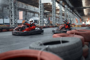İki kart yarışçısı viraja giriyor, ön manzara, kapalı alanda karting otomobil sporu. Lastik bariyeriyle yakın go-cart pistinde hız yarışı. Hızlı araç yarışması, yüksek adrenalin eğlencesi.