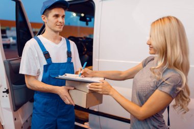 Üniformalı kurye arabadaki kadın müşteriye bir paket veriyor, teslimat servisi. Aracın yanında karton paket taşıyan adam, erkek teslimatı ve kadın, kurye ya da nakliye işi