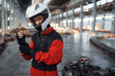 Kırmızı üniformalı, kasklı ve eldivenli bir Kart yarışçısı, kapalı alanda araba sporu yapıyor. Lastik engelli go-kart pistinde hız yarışı. Hızlı araç yarışması, yüksek adrenalin hobisi