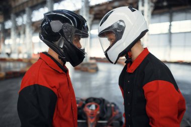 Miğferli iki yarışçı yüz yüze, kapalı mekanda araba sporu yapıyorlar. Lastik engelli go-kart pistinde hız yarışı. Hızlı araç yarışması, aktif hobi