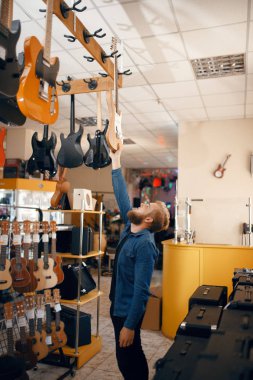 Müzik dükkanında akustik gitar seçen sakallı genç bir adam. Müzik aletleri dükkanında çeşitlilik, erkek müzisyen ekipman satın alıyor