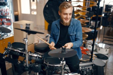 Müzik dükkanında bateri çalan sakallı genç bir müzisyen. Müzikal enstrüman dükkanında çeşitlilik, sanatçılar için profesyonel ekipman