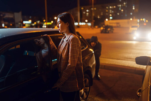 Female driver at the car, robber sneaking up behind, criminal, stealing. Hijacker victim in vehicle on parking. Auto robbery, automobile crime, hijack