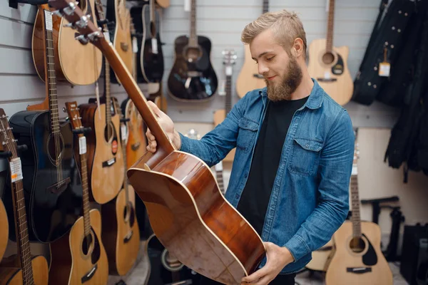 音楽店でアコースティックギターを選ぶ髭の若い男 楽器店での品揃え 男性音楽家購入機器 — ストック写真