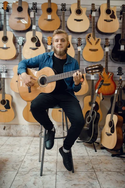 男性ギタリストは音楽店でアコースティックギターを演奏する 楽器店での品揃え 楽器を購入する音楽家 — ストック写真