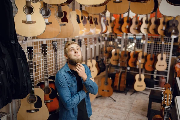 音楽店でアコースティックギターを選ぶ髭の若い男 楽器店での品揃え 男性音楽家購入機器 — ストック写真
