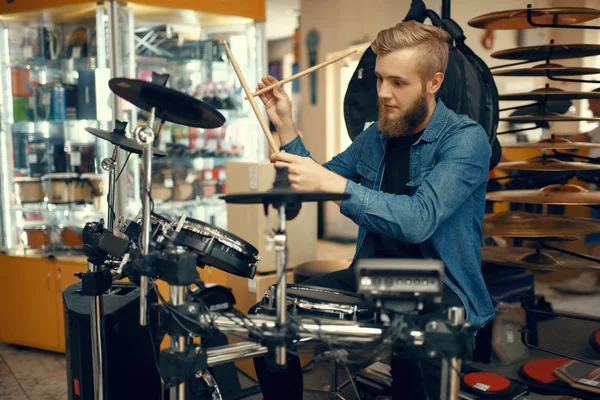 ひげを生やした若い音楽家が音楽店でドラムセットで演奏する 楽器店の品揃え 出演者のためのプロの機器 — ストック写真