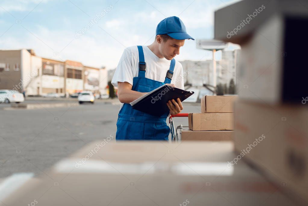 Deliveryman in uniform check parcels, delivery service. Man standing at cardboard packages in vehicle, male deliver, courier or shipping job