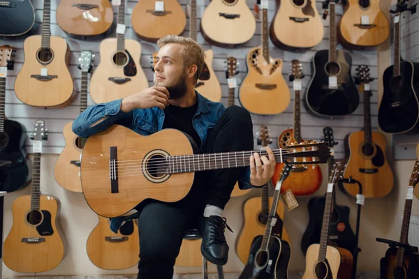 若い男は音楽店でアコースティックギターを演奏する 楽器店での品揃え 男性音楽家購入機器 — ストック写真