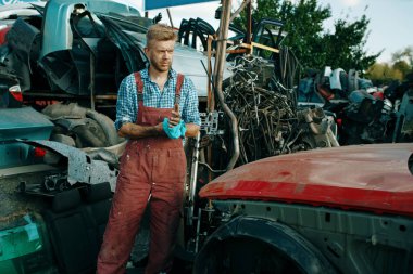 Araba hurdalığında havlusu olan bir erkek tamirci. Araba hurdası, araç hurdası, otomobil çöpü. Terk edilmiş, hasarlı ve ezilmiş nakliye, hurdalık