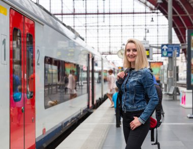 Sırt çantalı kadın turist tren istasyonunda trenini bekliyor, Avrupa 'ya gidiyor. Avrupa demiryolları, konforlu turizm ve seyahat
