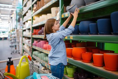 Rafta saksıları olan kadın müşteri, bahçe işleri için alışveriş yapıyor. Çiçekçilik, çiçekçi enstrümanı almak için mağazadan ekipman alan bir kadın.