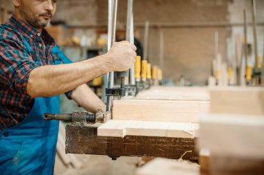 Üniformalı marangoz tahtayı mengeneyle, ahşap işçiliğiyle, marangozlukla kıskaçlıyor. Mobilya fabrikasında ahşap işleme, doğal malzemelerin üretimi