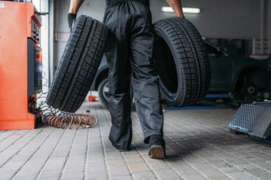 Tamircinin iki yeni lastiği var, tamirat servisi. İşçi garajda araba lastiği tamiri, atölyede profesyonel otomobil denetimi