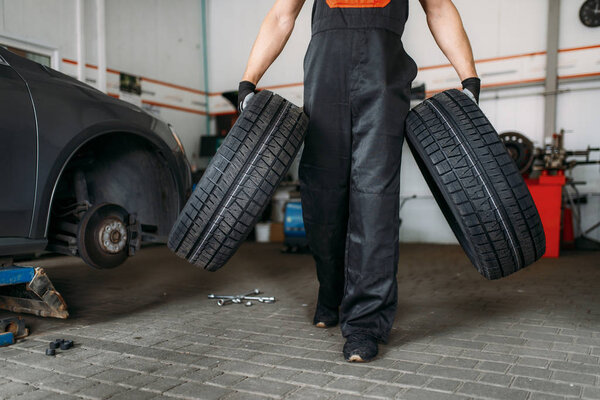 Auto mechanic holds two new tires, repairing service. Worker repairs car tyre in garage, professional automobile inspection in workshop