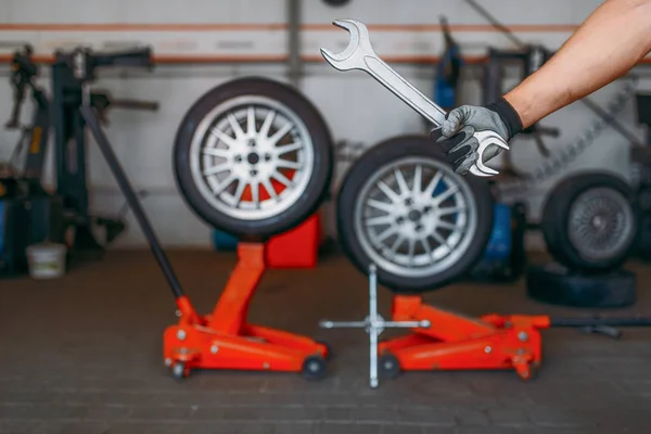 自動車整備士の手はレンチ タイヤサービスを保持します ワークショップでの専門的な自動車タイヤ検査 リフトジャックの車輪 バックグラウンド上のツールや機器の修理 — ストック写真