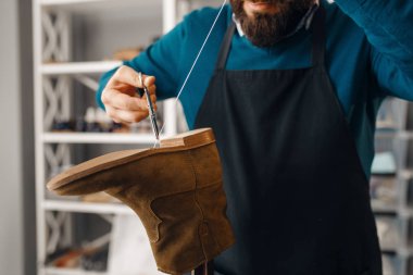 Shoemaker stitches the shoe, footwear repair service. Craftsman skill, shoemaking workshop, cobbler job