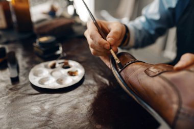 Shoemaker with brush tints shoes, footwear repair service. Craftsman skill, shoemaking workshop, master works with boots, cobbler clipart