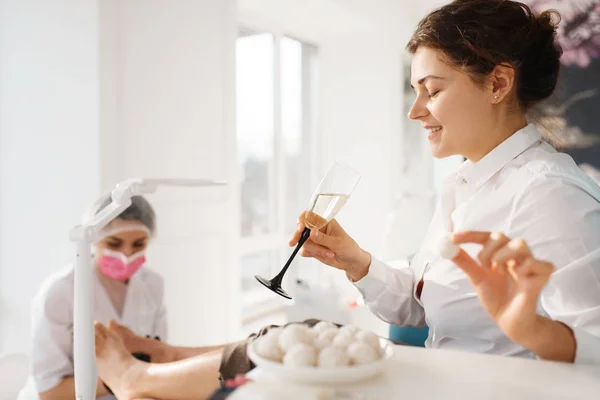 Woman with champagne relax in beauty salon, pedicure procedure. Professional beautician service, female customers, toenail and fingernail care in spa studio