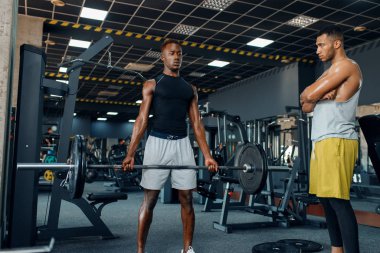 Kaslı adam ve antrenörü, spor salonunda halterle antrenman yapıyor. Spor kulübünde egzersiz, sağlıklı bir yaşam tarzı.