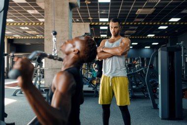 Kaslı adam ve eğitmeni, spor salonunda halterle egzersiz yapıyor. Spor kulübünde egzersiz, sağlıklı bir yaşam tarzı.