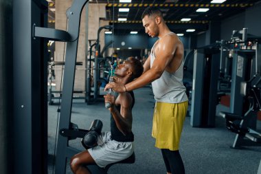 Kaslı adam ve eğitmeni, spor salonunda halterle egzersiz yapıyor. Spor kulübünde egzersiz, sağlıklı bir yaşam tarzı.