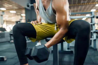 Spor kıyafetli kaslı bir adam ağırlık kaldırarak egzersiz yapıyor, spor salonunda antrenman yapıyor. Spor kulübünde egzersiz, sağlıklı bir yaşam tarzı.