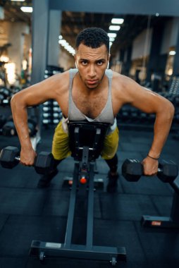 Spor kıyafetli kaslı bir adam, halterlerle egzersiz yapıyor, spor salonunda eğitim görüyor. Spor kulübünde egzersiz, sağlıklı bir yaşam tarzı.