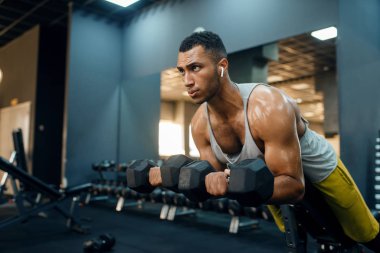 Spor kıyafetli kaslı bir adam, halterlerle egzersiz yapıyor, spor salonunda eğitim görüyor. Spor kulübünde egzersiz, sağlıklı bir yaşam tarzı.