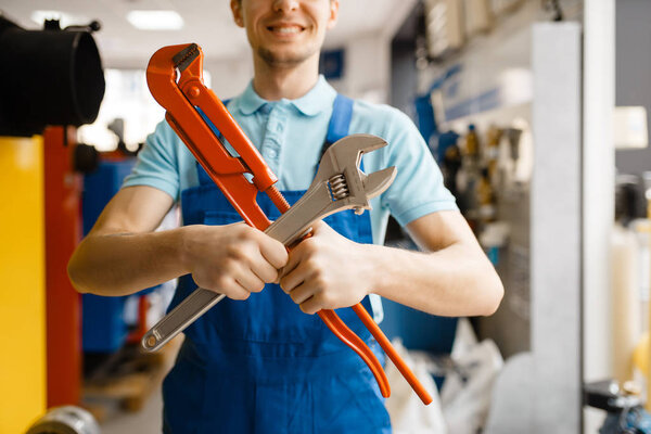 Plumber poses with pipe wrenches at the showcase in plumbering store. Man buying sanitary engineering tools and equipment in shop