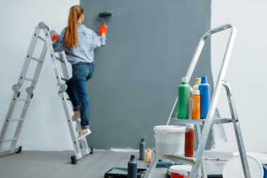 Female house painter paints walls indoor. Home repair, laughing woman doing appartment renovation, room decoration renovating