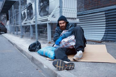 Male bearded beggar lies on city street. Poverty is a social problem, homelessness and loneliness, alcoholism and  drunk addiction, urban lonely